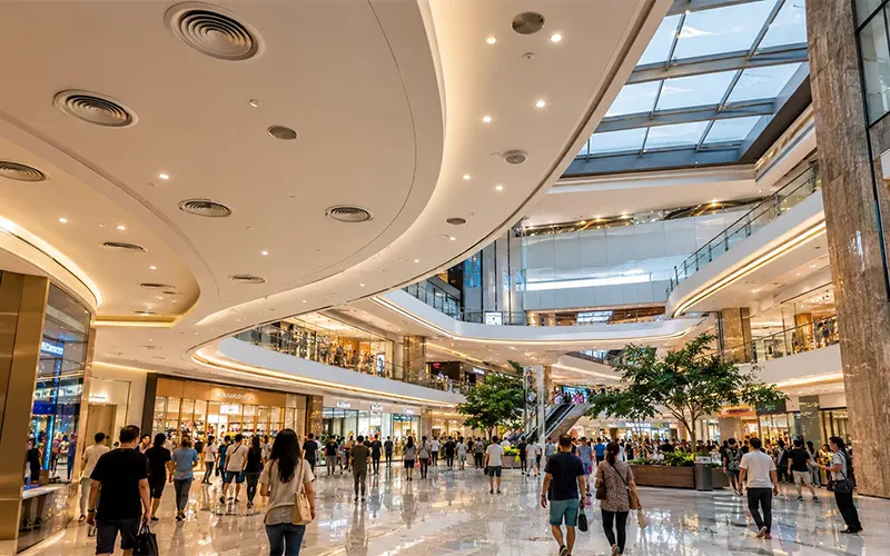 Modernes Atrium eines Einkaufszentrums mit hoher Besucherfrequenz, großen Innenbereichen, Glasdach und HLK-Luftauslässen für gewerbliche Luftfiltration.