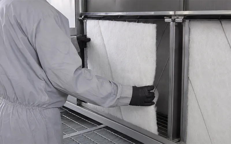 Wartungstechniker beim Austausch von Glasfaser-Farbnebelabscheider-Matten im Abluftbereich einer Lackierkabine.